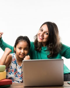 Indian girl studying with mother or teacher at study table with laptop computer, books and having fun learning